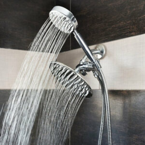 Dual shower heads on a single fixture, both spraying water against a tiled wall.