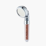 A handheld showerhead with a clear handle containing brown mineral beads for water filtration.