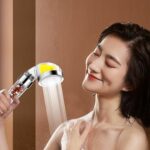 A woman with wet hair enjoys a shower, holding a filtered handheld showerhead with a large spray.