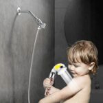 A young child showers with a detachable showerhead in a modern bathroom.