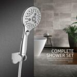 A modern silver showerhead on a gray tiled wall, with a white bathtub and plant. Text: "Complete Shower Set.