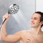 A person smiles while using a multi-spray handheld showerhead, with water streaming in the bathroom.