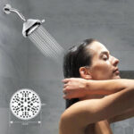 A dark-haired person showers under a wall-mounted 12 cm wide showerhead, with gray tiled walls in the background.