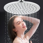 A person tilts their head back and closes their eyes under a large, round showerhead with water streaming down.