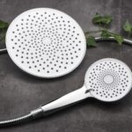 Two showerheads, one large and one small, with circular sprays on a dark surface, surrounded by green leaves.