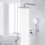 Modern bathroom: chrome rain showerhead and handheld shower on tiled wall, bathtub under bright window with sheer white curtains.