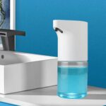 Automated soap dispenser with blue soap on a bathroom counter next to a sink and blue backdrop.