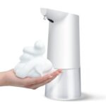 Hand holding foam under white automatic soap dispenser.