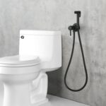 White toilet with wall-mounted black bidet sprayer on gray concrete wall.v