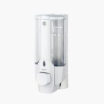 White wall-mounted soap dispenser with clear plastic container and push button.