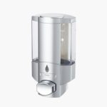 A silver wall-mounted soap dispenser with a clear container and bottom push-button for dispensing.