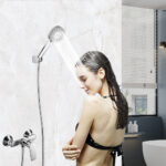 Someone showering under a wall-mounted showerhead in a modern bathroom, wearing a black bikini.