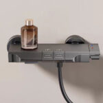 A sleek modern shower thermostat with a brown bottle on top.