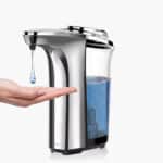 Рука под серебристым бесконтактным дозатором мыла с прозрачным, частично заполненным синим резервуаром для мыла.