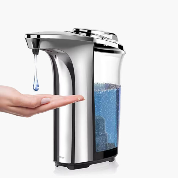 A hand under a silver touchless soap dispenser with a clear, partially filled blue soap reservoir.