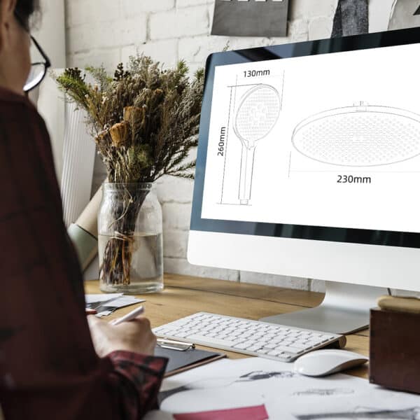 Persona en un escritorio con una computadora que muestra diagramas del cabezal de ducha de 9 pulgadas de Leelongs, útiles de oficina y flores secas cerca.