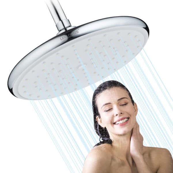 壁に取り付けられた丸いレインシャワーヘッドの下で、女性が目を閉じて微笑んでいます。シャワーヘッドから水が降り注いでいます。