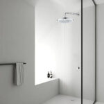 Baño minimalista con ducha a ras de suelo, cabezal de ducha de lluvia redondo grande, mampara de cristal, toallero y estante empotrado.