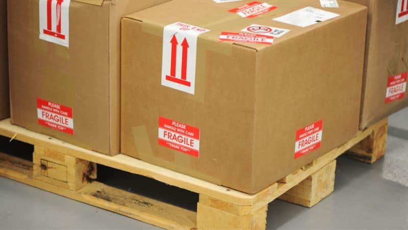 De grandes boîtes en carton « fragiles » sont empilées sur une palette dans un entrepôt.