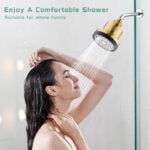 Shower head with gold finish releasing water onto woman enjoying shower experience in bathroom setting.