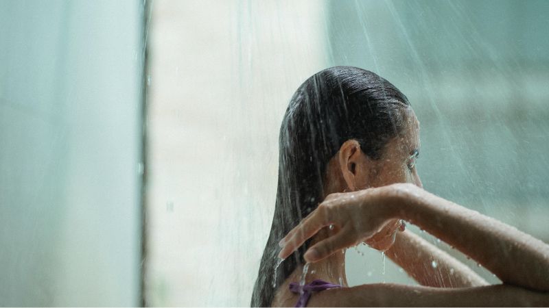 Gentlewoman taking a shower under running water, experiencing relaxation and self-care, showcasing modern bathroom and wellness lifestyle.