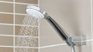 Close-up of a modern shower head with water spraying in a bathroom with beige tiled walls.