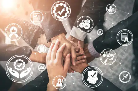 Business team holding hands together with digital icons representing teamwork, quality, and success overlaid.