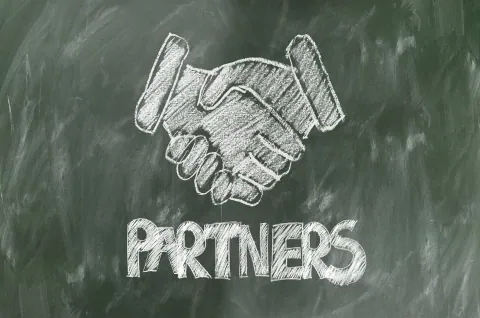 Chalk drawing of a handshake with the word 'PARTNERS' on a green chalkboard, symbolizing partnership and collaboration.