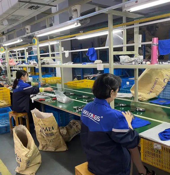 Workers assembling electronic devices on a production line in a factory setting with tools and components.